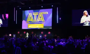 Large conference hall with a speaker on stage at the AT A 2026 Apprenticeship & Training Awards, a bright purple-lit backdrop and a large screen displaying the AT A logo.