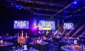Award ceremony venue with a lit stage and large ATTA 2026 screens, blue lighting, and dining tables set for guests in the foreground.