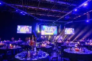 Banquet hall with round tables, candle centerpieces, and a stage featuring ATTA 2026 on large screens.