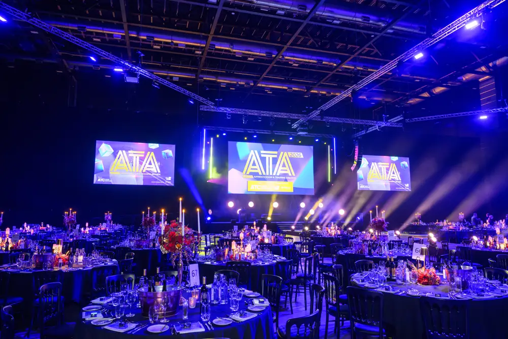 Banquet hall with round tables, candle centerpieces, and a stage featuring ATTA 2026 on large screens.