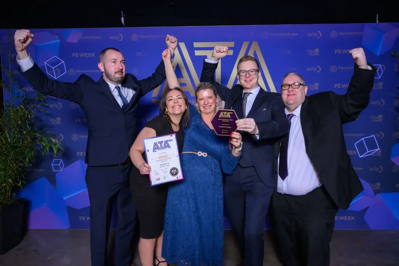 Winners celebrating with arms raised, holding their ATA trophy and certificate in front of the awards backdrop.